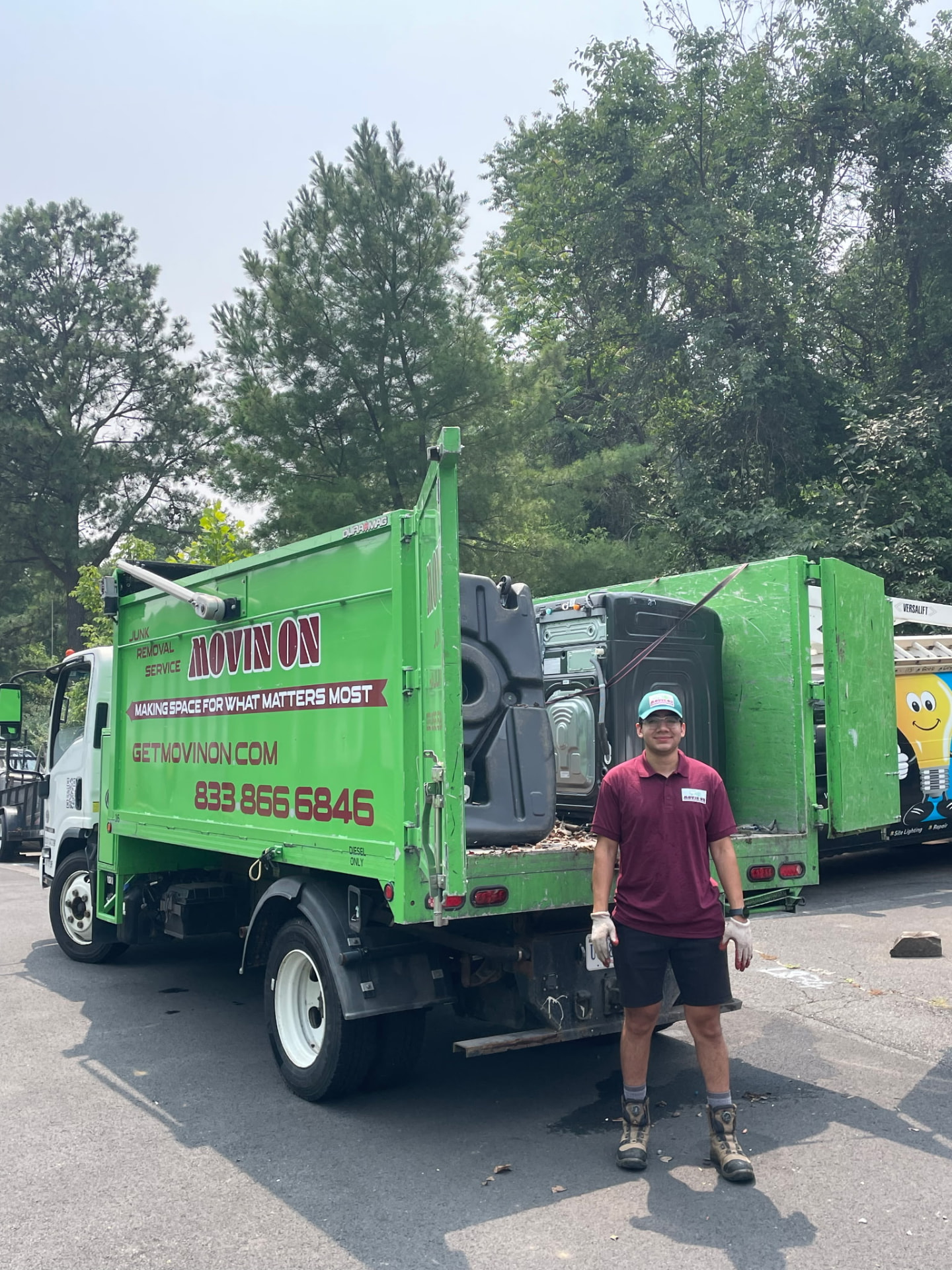 Movin On crew member standing beside the green Movin On junk removal truck loaded with old appliances